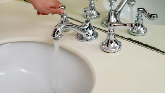 Hand operating a chrome faucet with running water in an elegant bathroom setting.